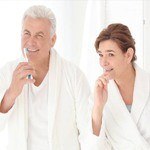 Older man and woman brushing teeth together after implant denture placement