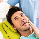 Man on dental chair holding cheek in pain before TMJ therapy