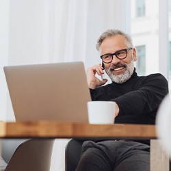 Man with glasses smiling while working on laptop
