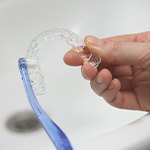 Patient using toothbrush to clean aligners in sink