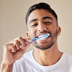 Man in white shirt smiling while brushing teeth