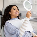 Woman smiling at reflection in handheld mirror