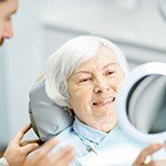 Female patient smiling in mirror after All-on-4 dental implant placement