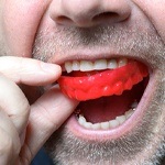 close up of a man putting a red mouthguard in his mouth
