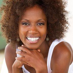 Lady in white tank top smiling after GLO teeth whitening treatment