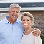 Older couple smiling outside of their house with brick