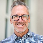 Older man smiling with glasses while wearing a checkered collared shirt