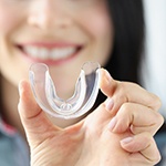 Woman with dental implants in Grapevine, TX holding a mouthguard 