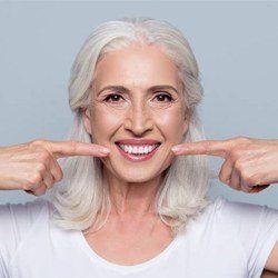 Older woman pointing to beautiful smile after implant denture placement