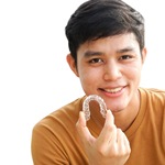 A male teenager holding an Invisalign aligner and wearing a yellow shirt