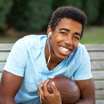 A young male teenager sitting on a bench wearing headphones and holding a football