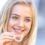 A female teen smiling and preparing to insert an Invisalign aligner into her mouth