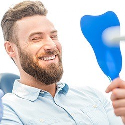 Man looking at smile in mirror after Invisalign treatment