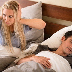 A man snoring in need of sleep apnea treatment and a woman with her hands over her ears