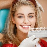 A dentist comparing tooth shades against a woman’s smile