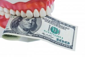 A set of false teeth holding a one-hundred dollar bill.